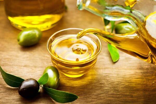 Olive Oil. Bottle pouring Virgin Olive Oil in a bowl close up. O
