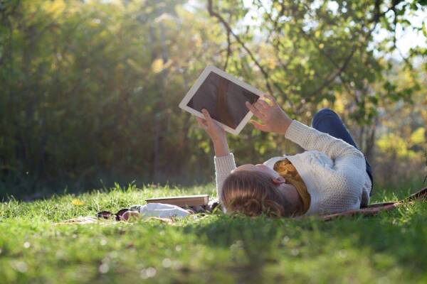 Woman Lying On Bedding On Green Grass With Ipad During Picknic I